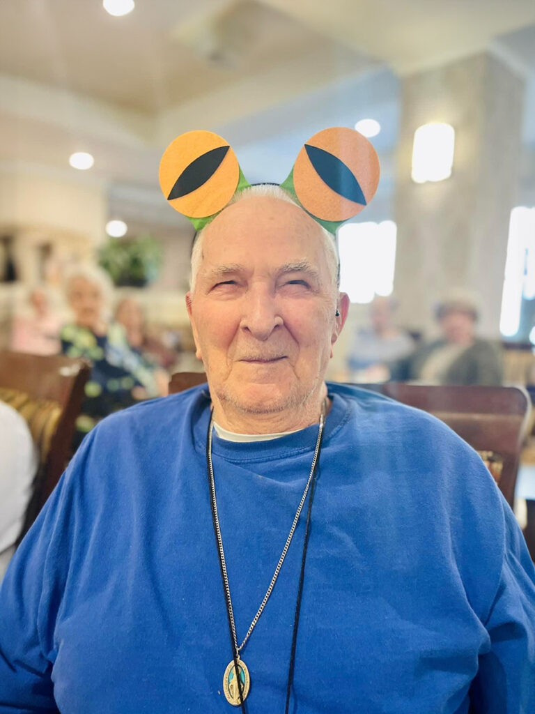 Larry, an elderly man in a blue shirt, and fun frog eye headband at a community event.