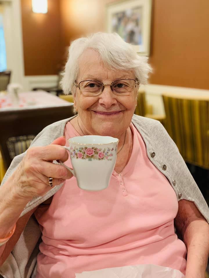 A current photo of Dottie smiling in a pink shirt and holding a tea cup with detailed pink flowers.