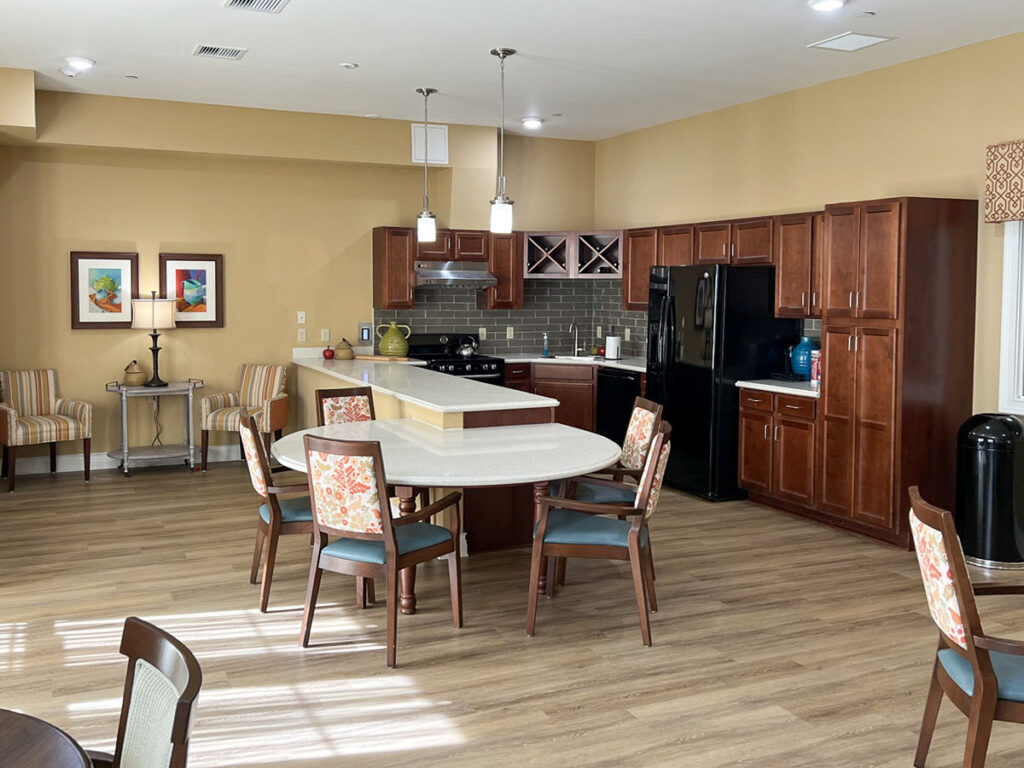 Kitchen area at the Boulevard of Saint Charles Senior Living, with a central island, chairs, wooden cabinets, and a cozy seating nook.