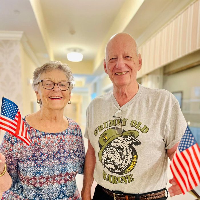 A cheerful couple celebrates Independence Day, holding small American flags. The woman wears a patterned blue and red top, while the man sports a 