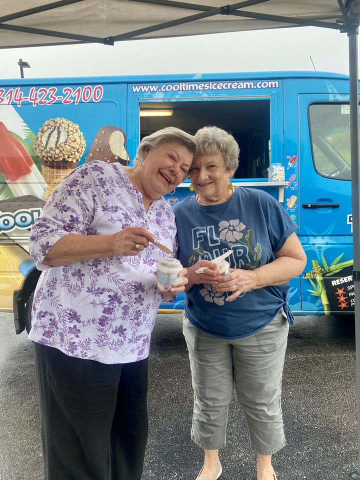 Two senior living community residents smiling and enjoying ice cream in front of a colorful ice cream truck.