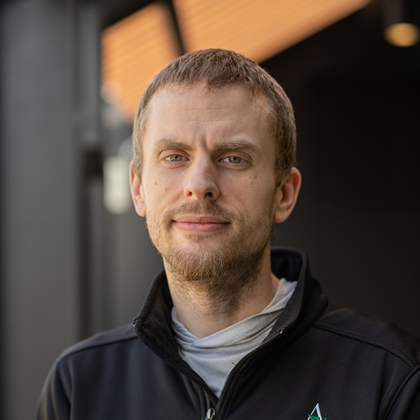 Derek Winning, Culinary Director at The Boulevard Senior Living of Saint Charles, pictured in a black zip-up jacket, standing confidently in an outdoor setting with soft lighting and blurred architectural elements in the background.