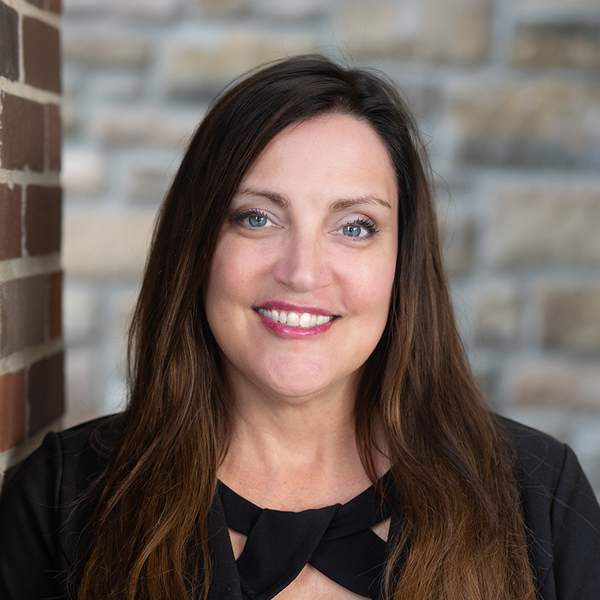 Kelly Arnold, Executive Director at The Boulevard Senior Living of Saint Charles, smiles in front of a brick wall, wearing a black top and long brunette hair.