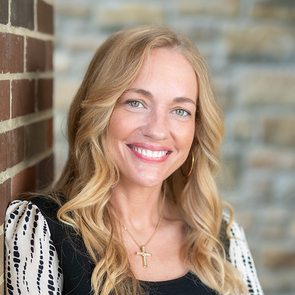 Mollie Levine, Memory Care Director at The Boulevard Senior Living of Saint Charles, smiles in front of a brick wall, wearing a cross necklace and black top.