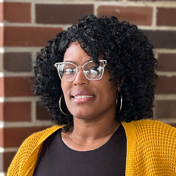 Trneal Reading, Memory Care Director at The Boulevard Senior Living of Saint Charles, smiling while standing outdoors against a brick wall, wearing glasses and a cardigan.
