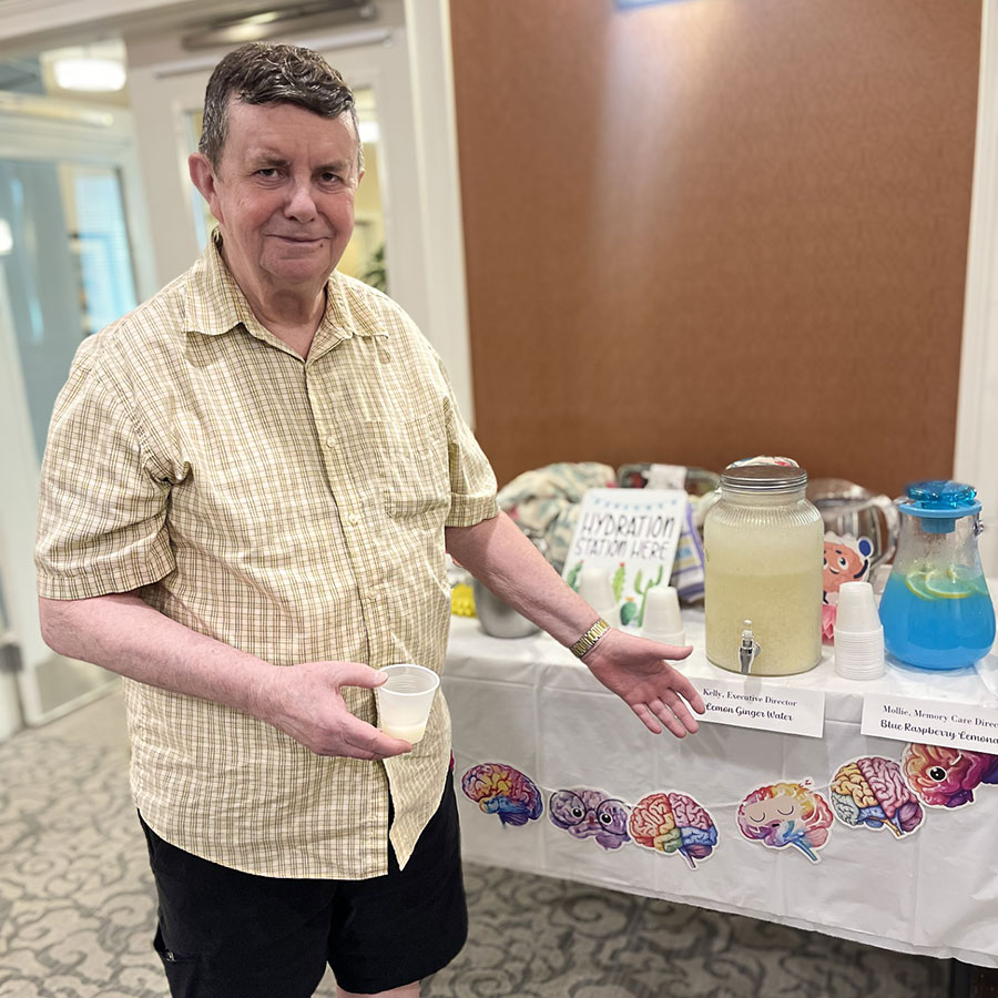 A man smiles, gesturing toward a table set with lemonade during an event.