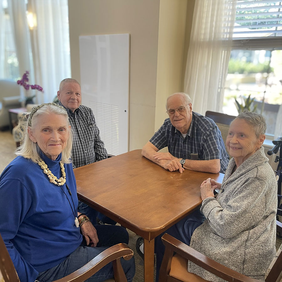 Four senior friends smile around a table at The Boulevard Senior Living of Saint Charles.