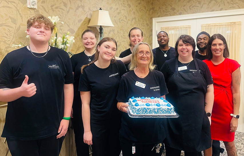 Team members at The Boulevard Senior Living St. Charles smile together, one woman holding a cake.