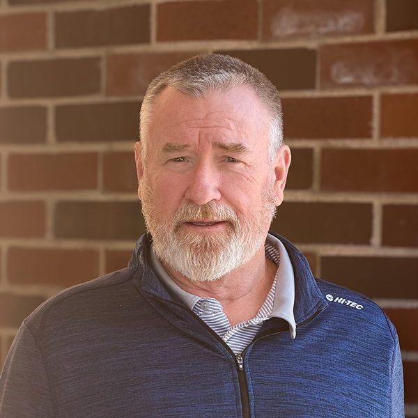 Robert “Bob” McKeon, Plant Operations Director at The Boulevard Senior Living of Saint Charles, posing in a professional headshot, wearing a blue quarter-zip, with a brick wall background.