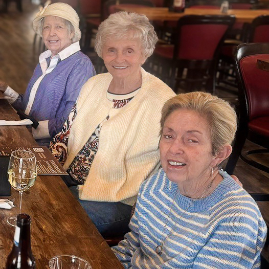 Three senior women smile while dining out.