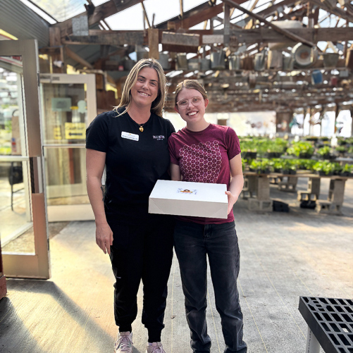 A woman on the Arrow team smiles alongside a member of a local greenhouse's team with a gift.
