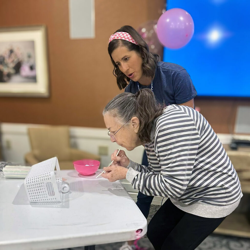 A woman looks on while a senior woman engages in a game during a community event.
