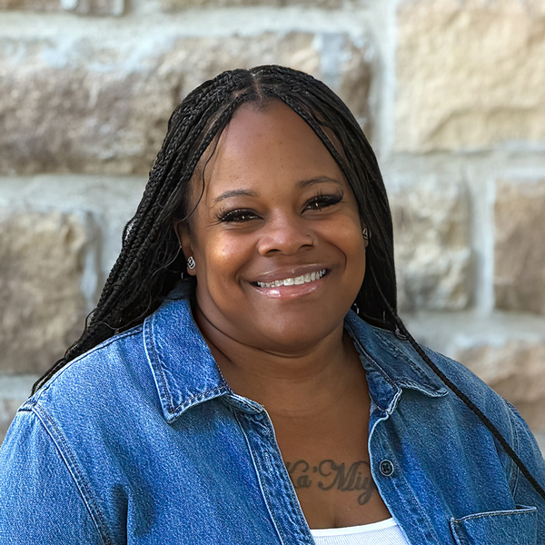 Brittany Crawford, Memory Care Director at The Boulevard Senior Living of St. Charles, smiling in a professional headshot with long braids, a denim button-up shirt, and a light stone wall background.