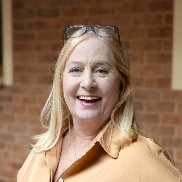 Christy Dickerson, Resident Services Director at The Boulevard Senior Living of St. Charles, smiling in a professional outdoor headshot with blonde hair, glasses resting on her head, a tan blouse, and a softly blurred brick background.