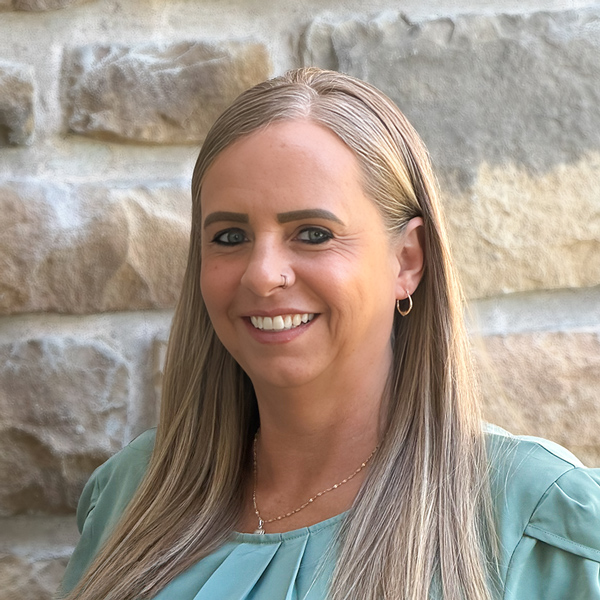 Melissa Schuff, Senior Living Coordinator at The Boulevard Senior Living of St. Charles, smiling in a professional headshot with long blonde hair, hoop earrings, a light green blouse, and a light stone wall background.